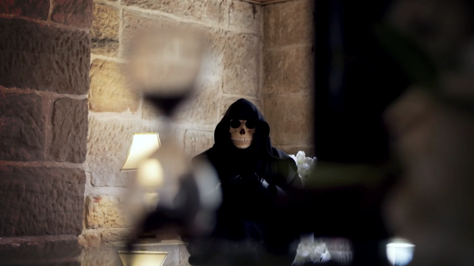 A hooded skeletal figure seen through hourglasses and stone archways