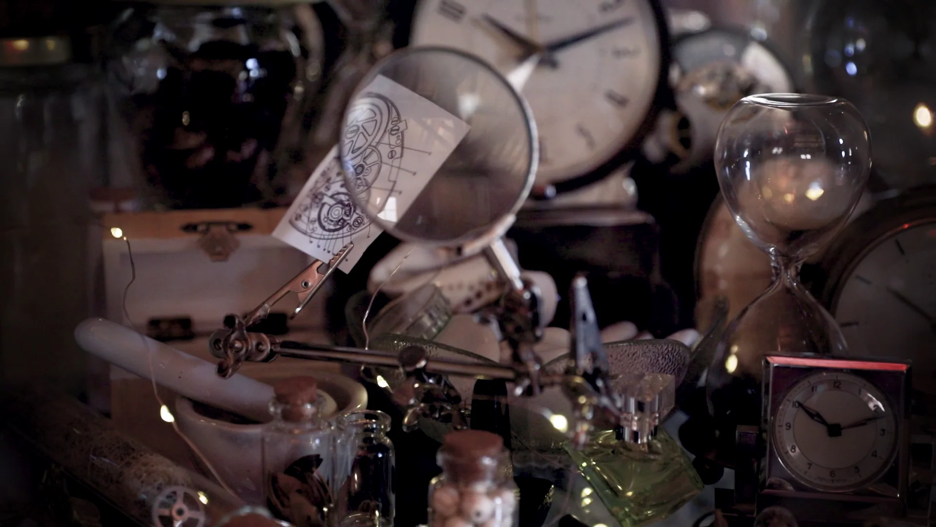 Clocks, magnifying glasses, glassware and mechanical drawings arranged inside the room