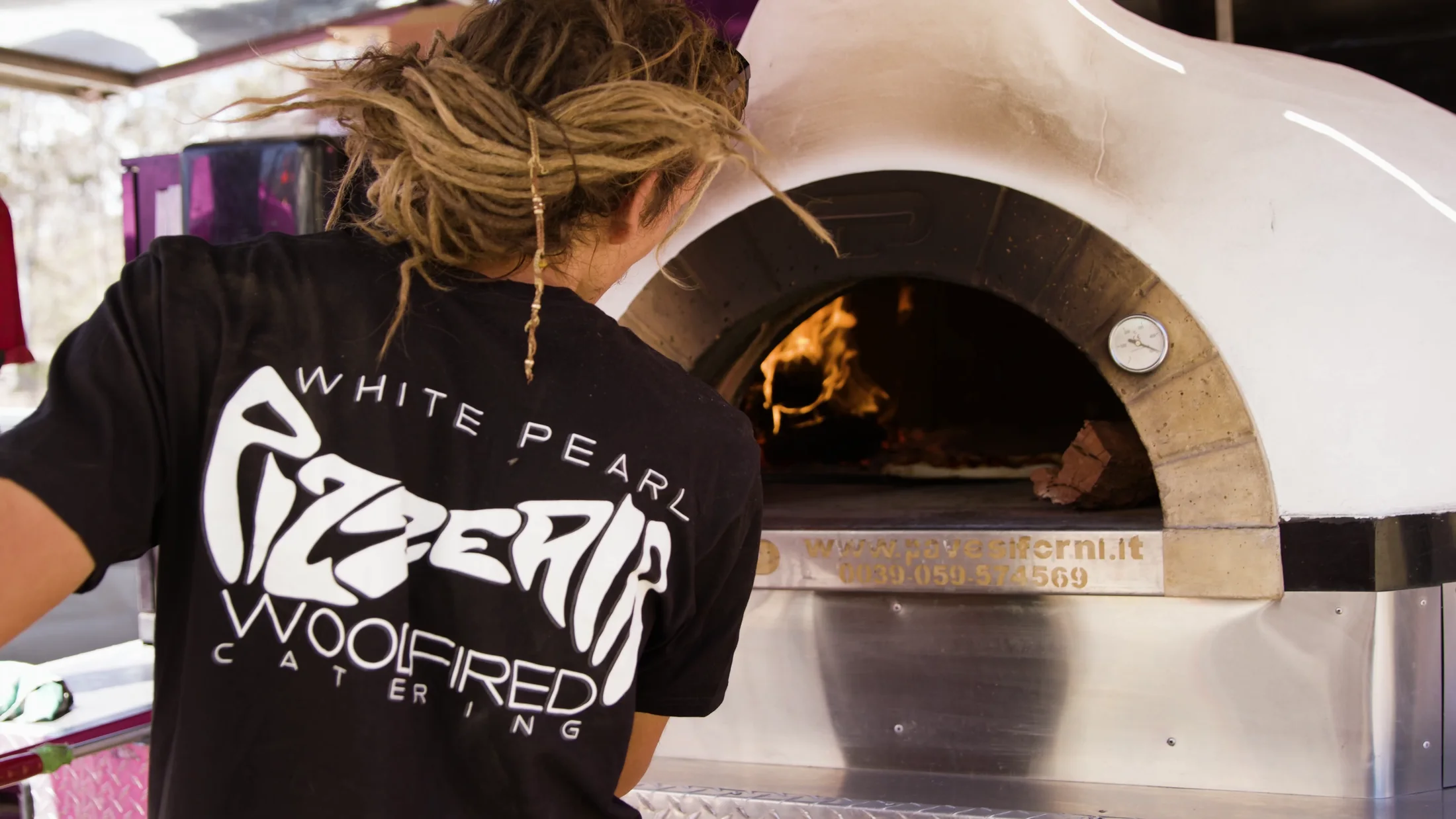 A pizza being placed into White Pearl's mobile wood-fired oven