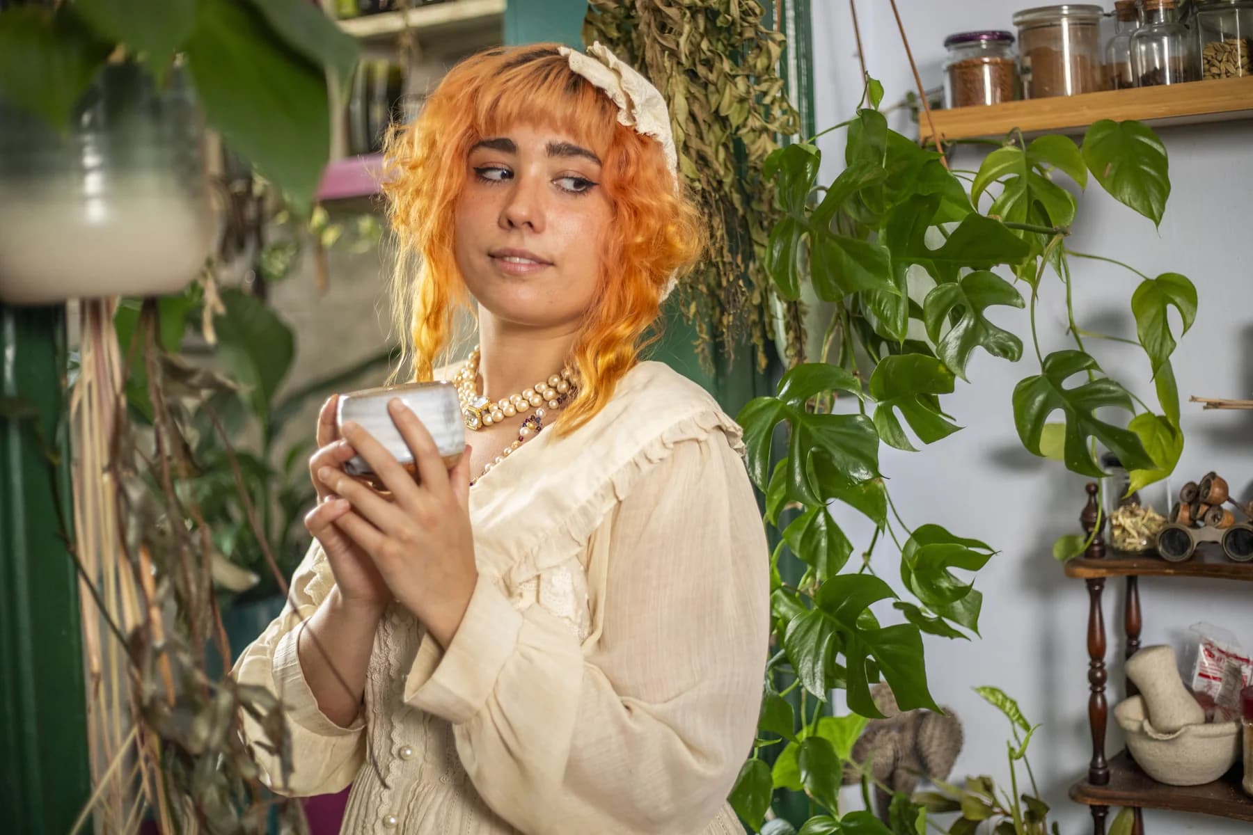 Inge holding a cup among hanging plants