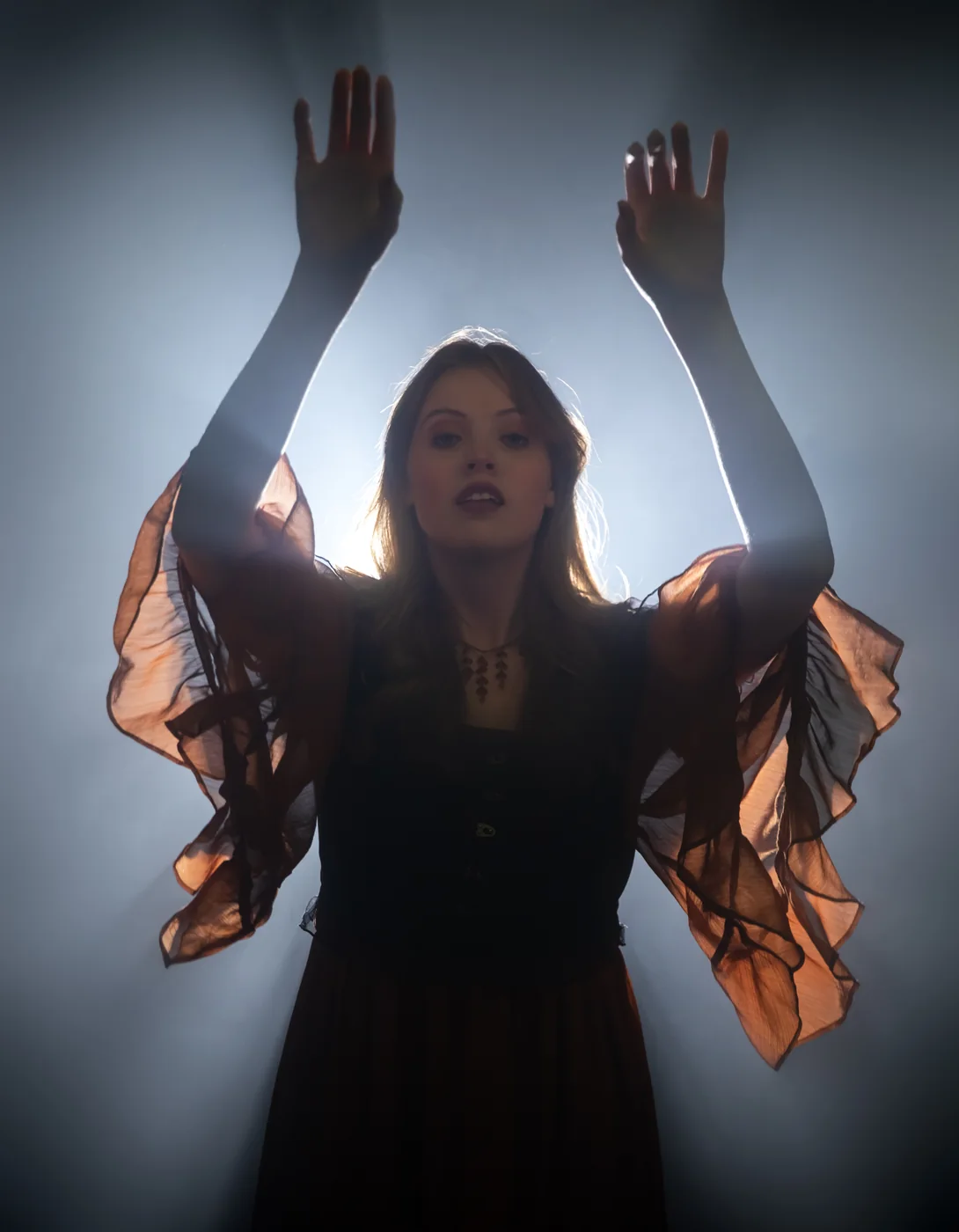 Close portrait framed by raised arms and white backlight